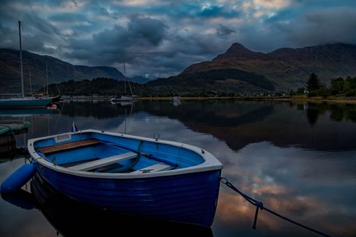 A roawing boat on the water in Scotland, with mountains in the background on a clouded day