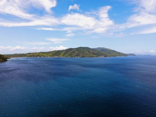 An aerial view of the blue sea and green mountains on a sunny day