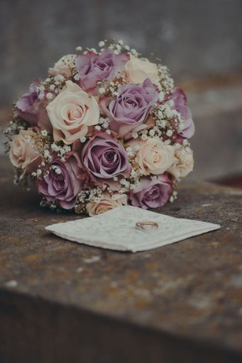 A pair of golden wedding rings on white fabric by bouquet of beautiful roses on the table