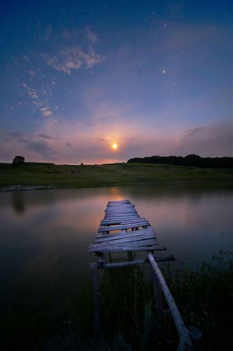 A dramatic scenery of a late sunset in the sky over the lake and a broken wooden pier