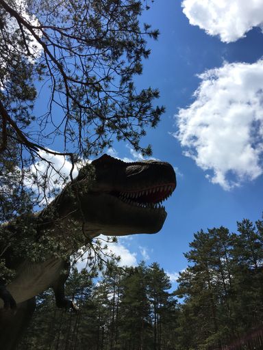 A vertical low angle shot of a dinosaur statue against a blue cloudy sky in a park