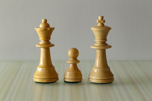 A closeup shot of a white chess pawn between the kind and queen figures