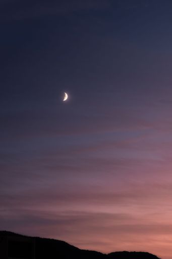 A vertical shot of the crescent moon in the sky at sunset