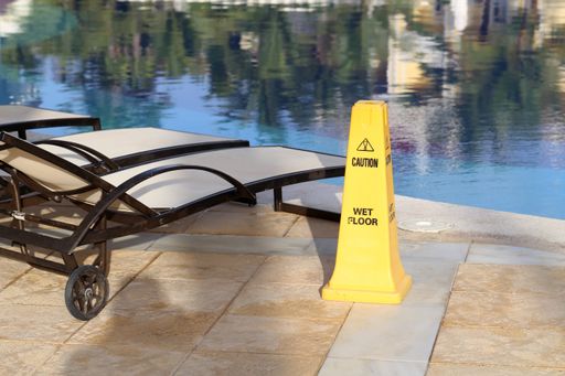 A yellow "Caution, wet floor" sign near a pool under the sunlight