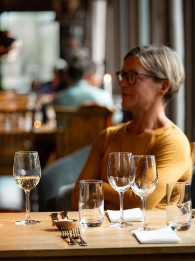 A vertical shot of a Caucasian woman sitting in a restaurant and glass of wine on the table