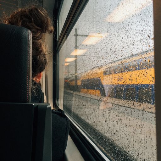 A female sitting in the train beside a window covered with water drops - post-break-up depression mood