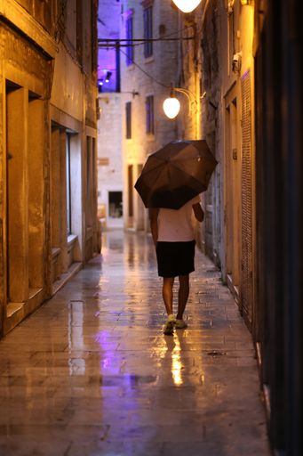 A vertical shot of a male with an umbrella walking in rainy weather