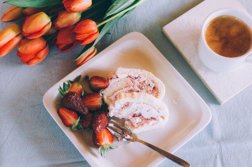 A high angle closeup shot of a delicious strawberry dessert and a cup of coffee next to orange tulips