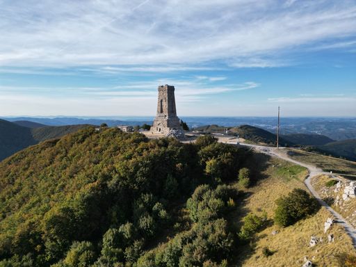 An aerial view of the Shipka Monument on top of a mountain surrounded by lush green foliage