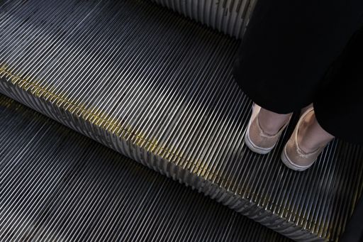 A female's feet standing on a metal escalator staircase shot from above