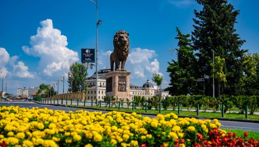 A beautiful view of a giant lion sculpture in the middle of a road surrounded by greenery in Skopje