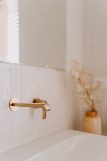 An interior shot of a modern bathroom featuring white porcelain fixtures contrasted with gold accents
