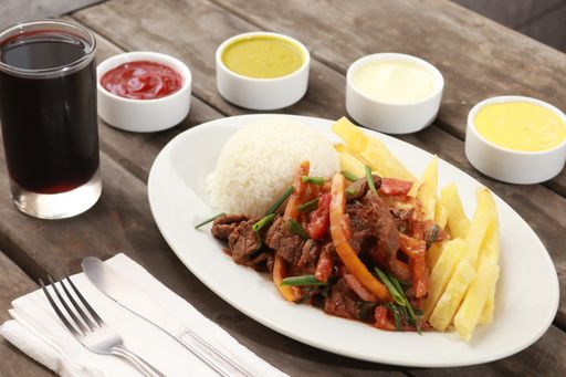 A shot of meat with vegetables, potatoes fries, rice garnish, and sauces