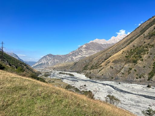 A scenic shot of a lake in the valley between two hills, with a mountain range in the background on a sunny day