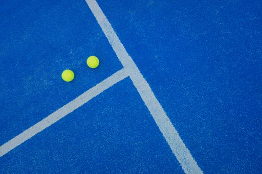 A drone shot over of two balls near the net of a paddle tennis blue court