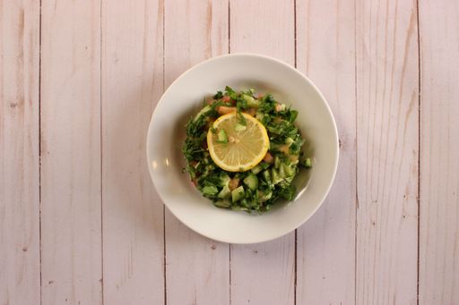 A top view of green salad with lemon slice on it, on wooden surface
