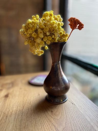A closeup of yellow immortelle flowers in a vintage vase
