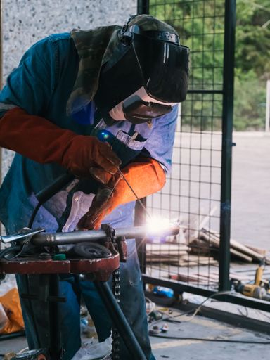A vertical shot of a man wearing a mask welding metal handrails - concept of craft metal production