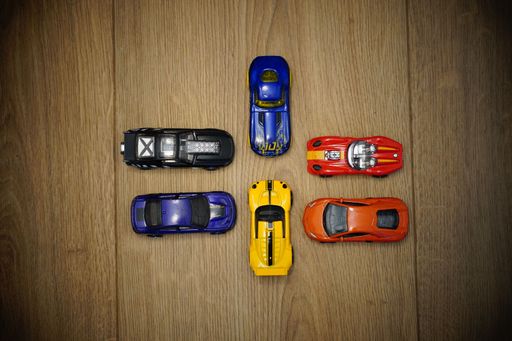 A group of multi-color toy cars on a wooden surface