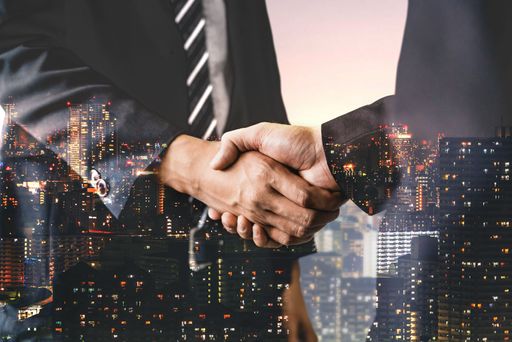 A double-exposure shot of business people shaking hands showing success of a deal - teamwork concept