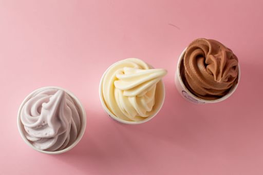 A top view of chocolate, vanilla, and taro soft serve ice cream on a pink table
