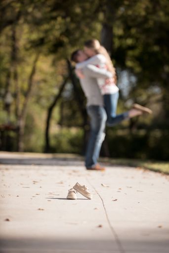 A vertical shot of a pair of kid shoes with a young couple holding and kissing in the background