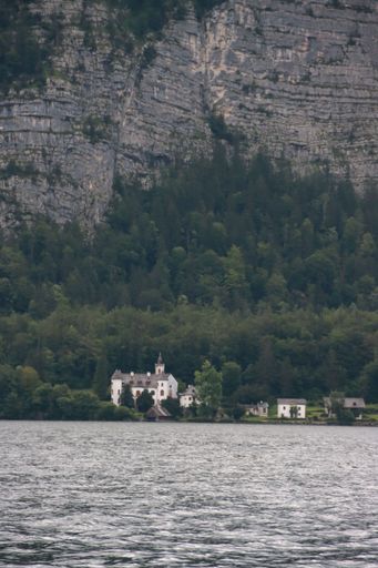 A vertical shot of fishermen on a boat near by a coast with high cascade forest trees