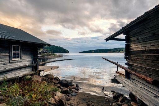 A scenic shot of old wooden houses and stones in front of a lake in gloomy weather