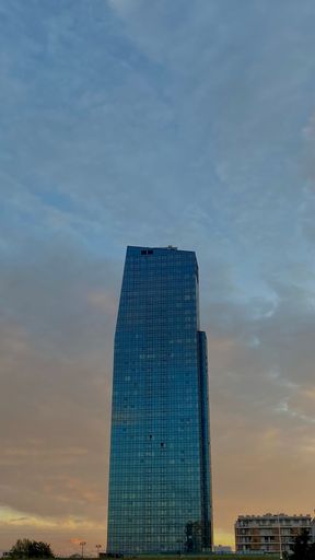 A vertical shot of a modern skyscraper with glass windows against a cloudy sky at sunset