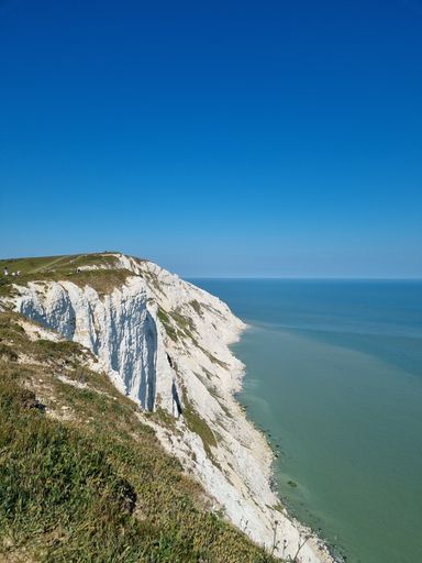 A gorgeous vertical shot of the Seven Sisters cliff in England with a calm sea under a cloudless blue sky on a sunny day