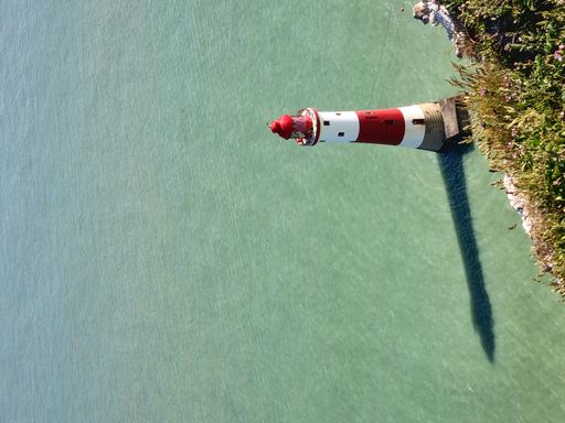 A vertical low angle shot of a lighthouse at Seven Sisters in England with a pale green sea on a sunny day
