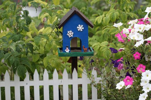 A closeup of a blue birdhouse behind a white fence