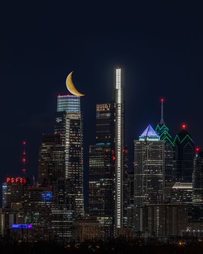 The yellow crescent moon over illuminated Philadelphia skyline at night