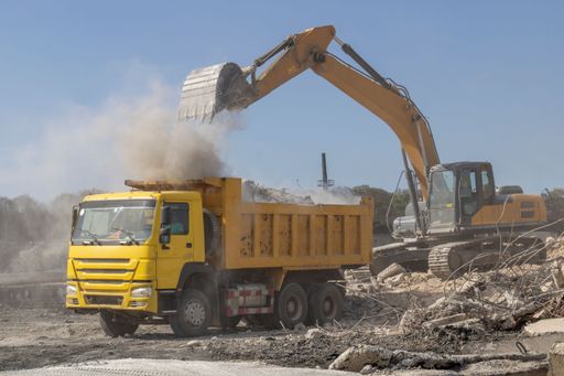 An excavator loading rubble into a dump truck at a construction site
