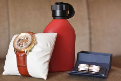 A closeup shot of a fancy watch, perfume and cufflinks on a wooden surface