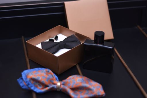 A closeup shot of a perfume, a bow tie and cufflinks in a box