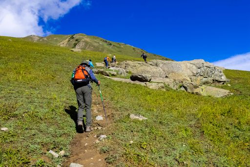 A closeup shot of a group of hikers climbing a green mountain under the blue sky