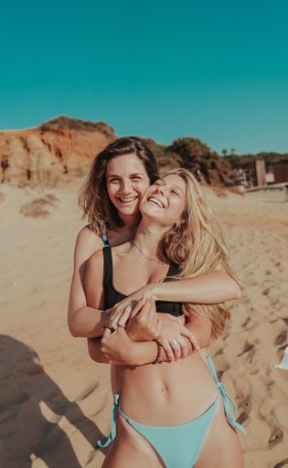 A vertical shot of beautiful young female friends hugging each other on a beach