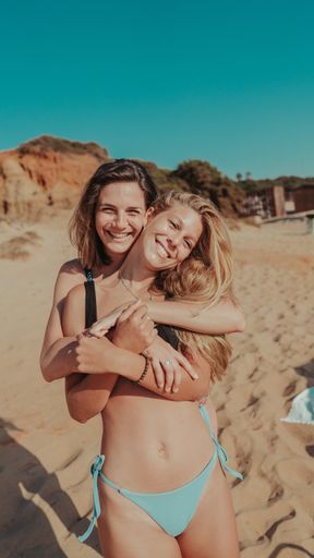 A vertical shot of beautiful young female friends hugging each other on a beach