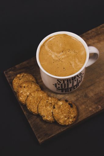 A vertical shot of a cup of coffee with some cookies on a wooden tray in a dark studio