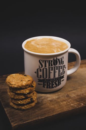 A vertical shot of a cup of coffee with some cookies on a wooden tray in a dark studio