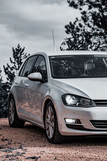 A white Volkswagen golf parked on street surrounded by trees
