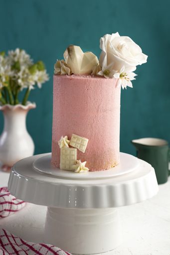 A vertical closeup shot of a small fancy pink cake with white roses on a tray