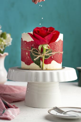 A vertical shot of a small fancy cake with a red rose on a white tray