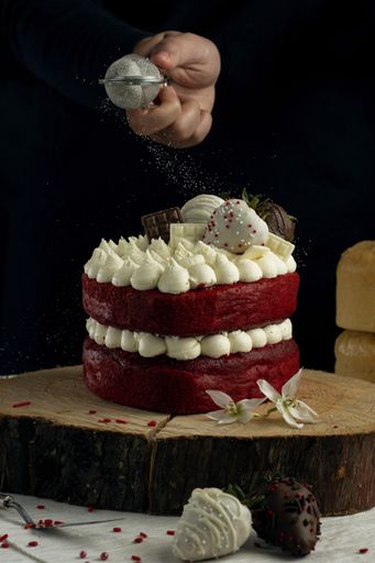 A vertical shot of a person pouring sugar powder on a fancy small red velvet cake with white cream