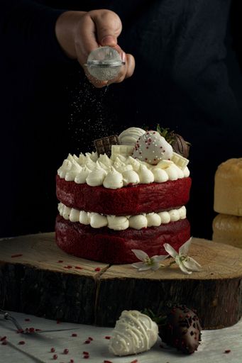 A vertical shot of a person pouring sugar powder on a fancy small red velvet cake with white cream
