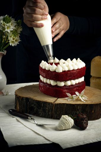 A vertical shot of a person adding white cream on a red velvet cake