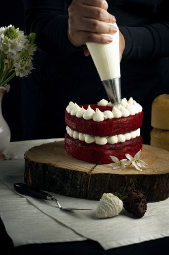 A vertical shot of a person adding white cream on a red velvet cake