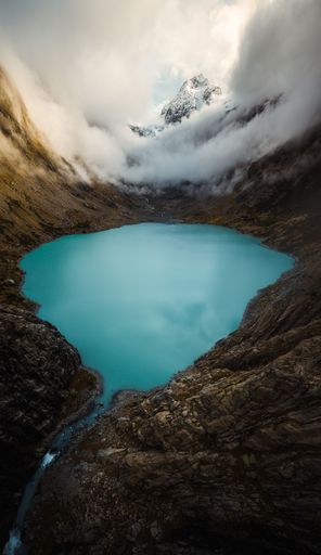 A vertical shot of a clear blue lake surrounded by the mountains and clouds during the daytime