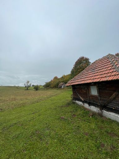 A vertical shot of rural wooden cottages in a large green field in Sjenica, Serbia